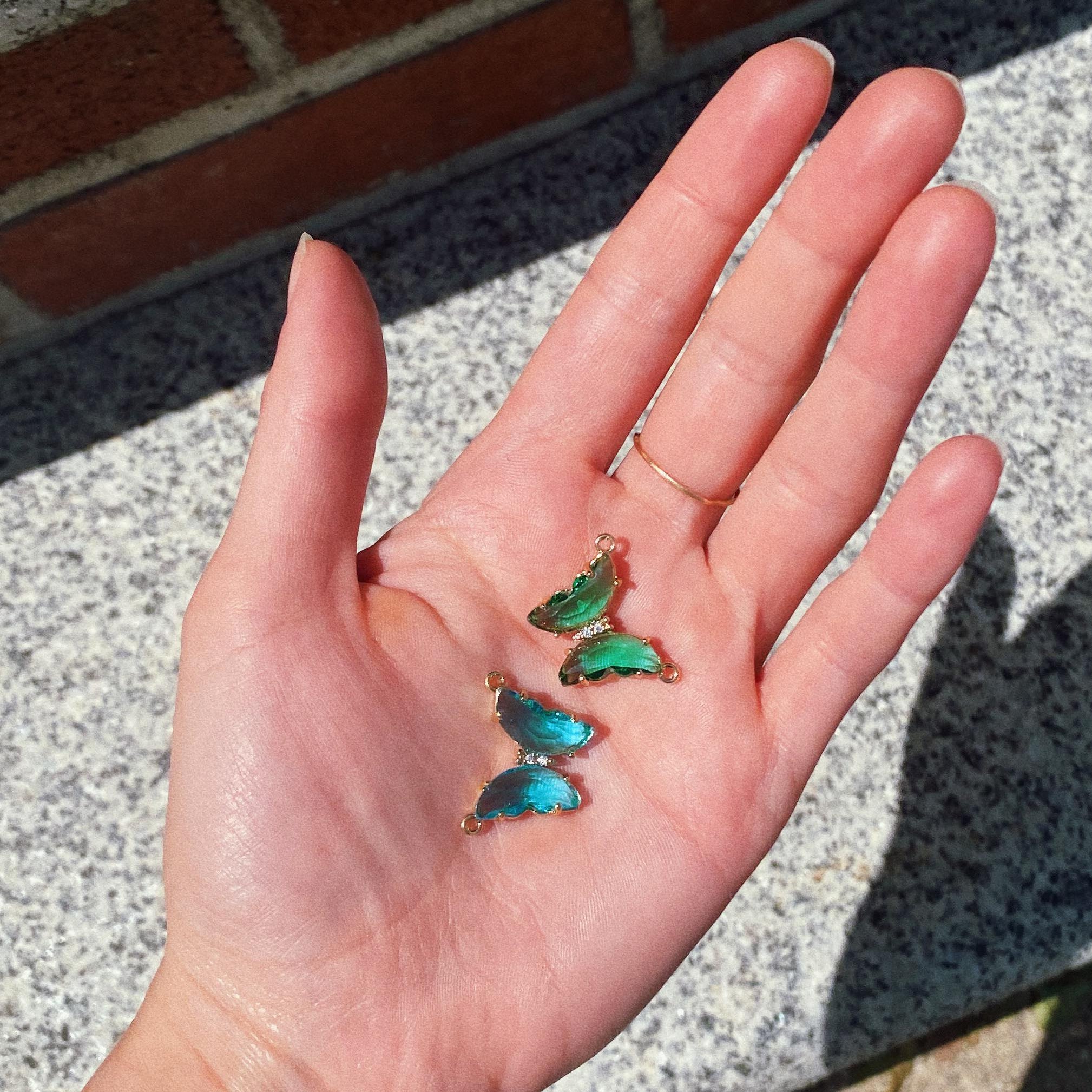 Picture of a woman holding 2 butterfly connector pendants, one green and one aqua.