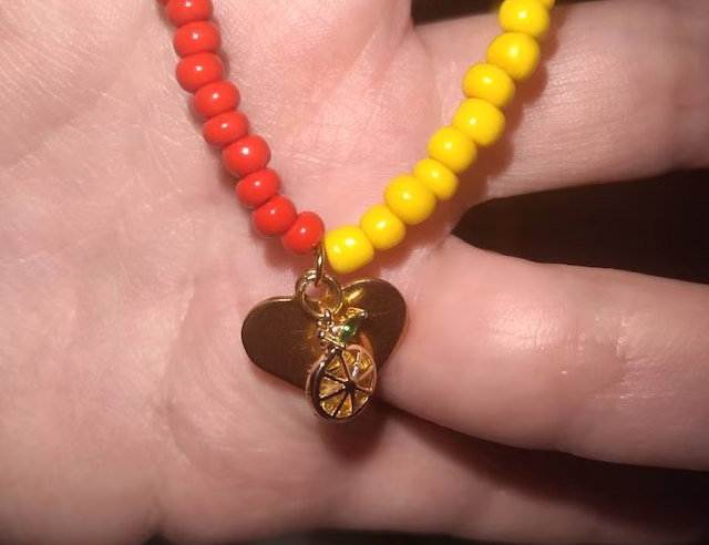 A woman holding a half yellow, half red beaded necklace with a gold orange fruit charm