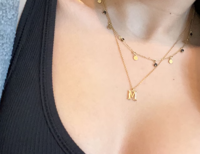 A woman in a review wearing a gold necklace with a gold letter 'M' charm/pendant.